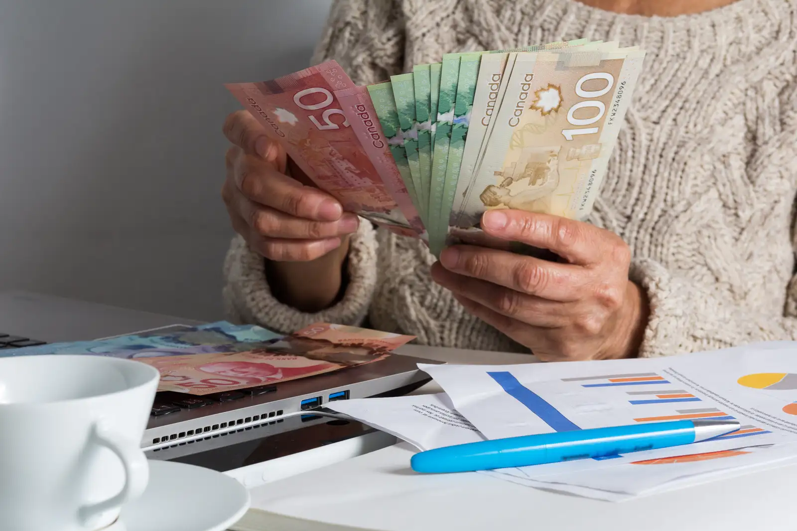 Kanada doları banknotlarını sayan eller; masada hesap çizelgeleri